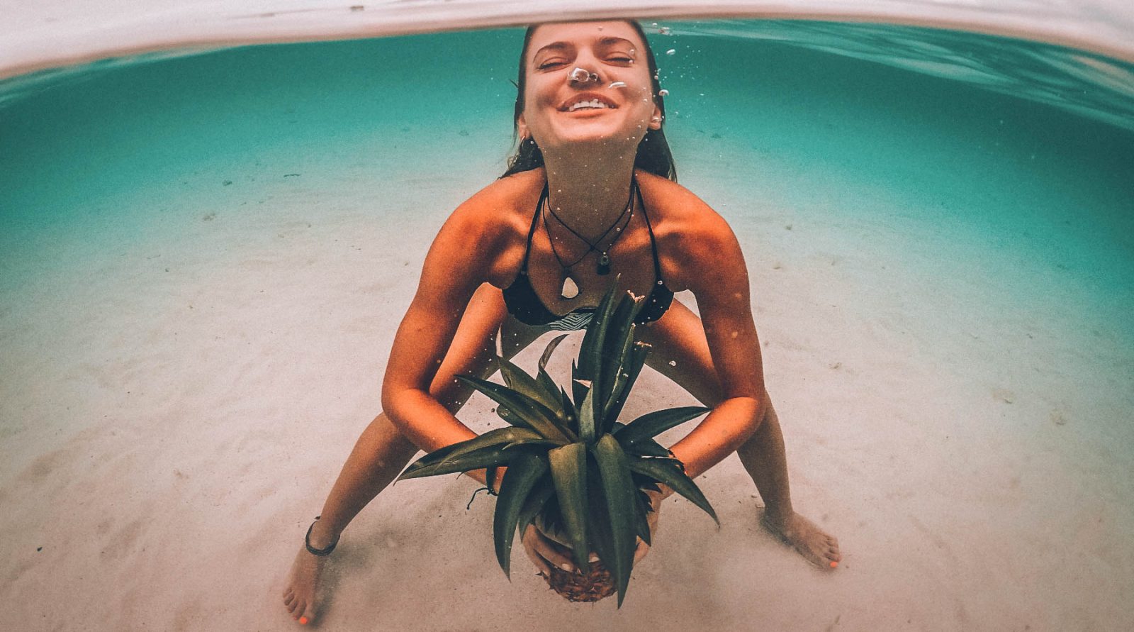 A girl under the water with a pineapple