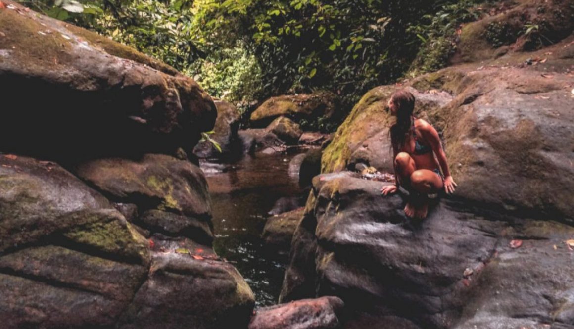 A girl sitting on the big rock next to the waterfalls