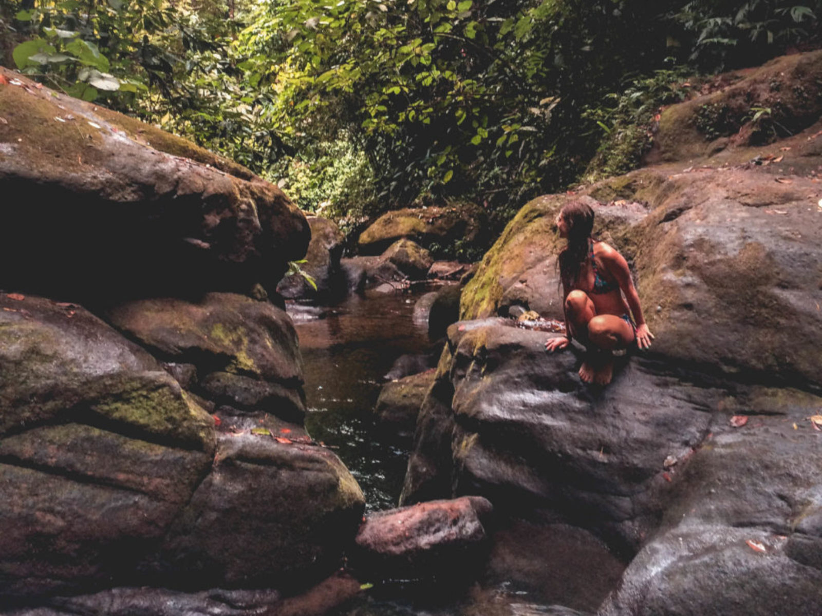 A girl sitting on the big rock next to the waterfalls