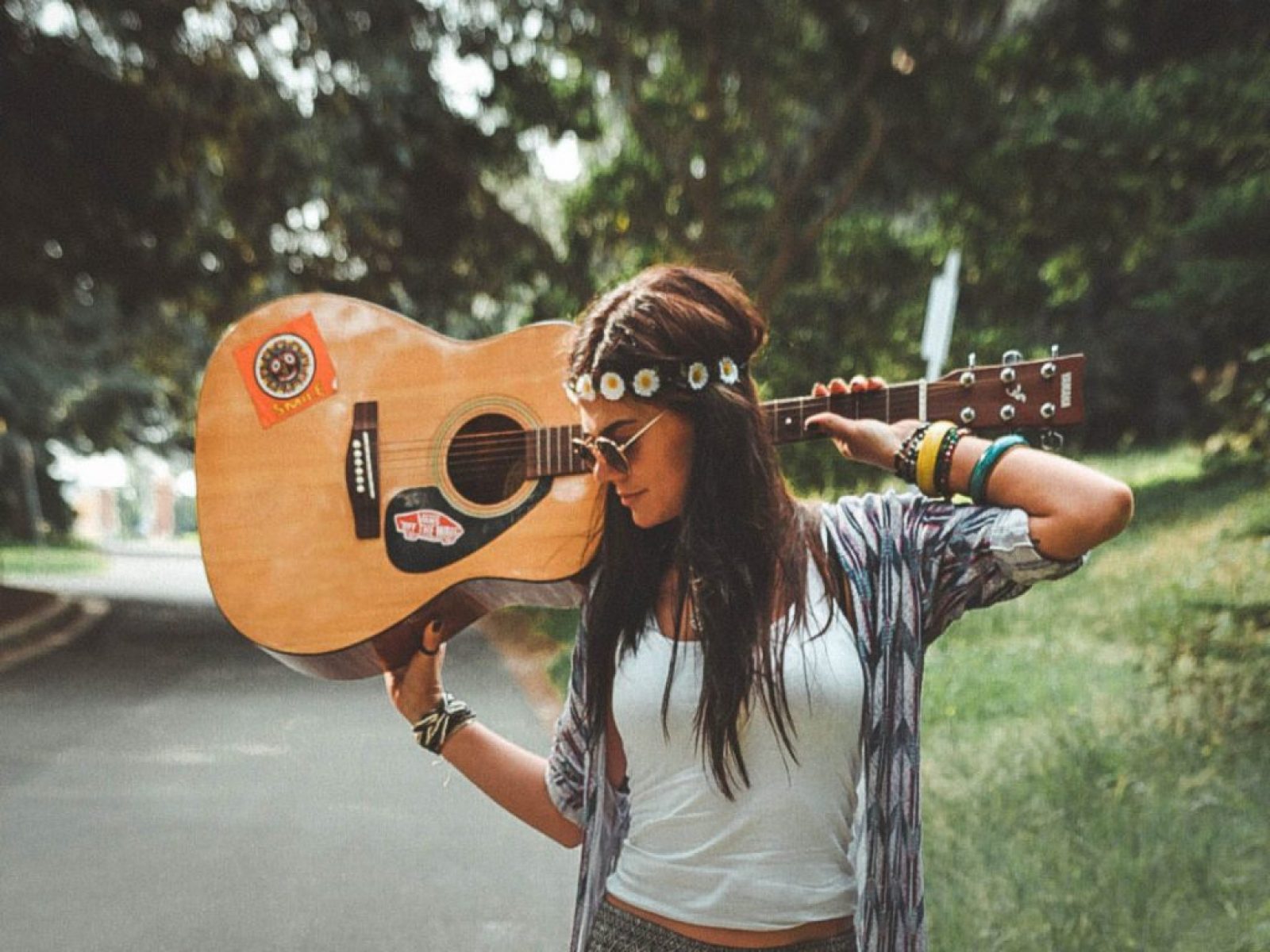 A girl wearing boho clothes and walking with a guitar